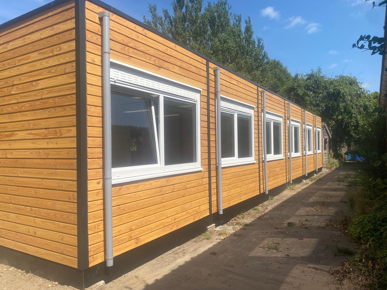 Langgerekt schoolgebouw met houten gevelbekleding en witte kozijnen