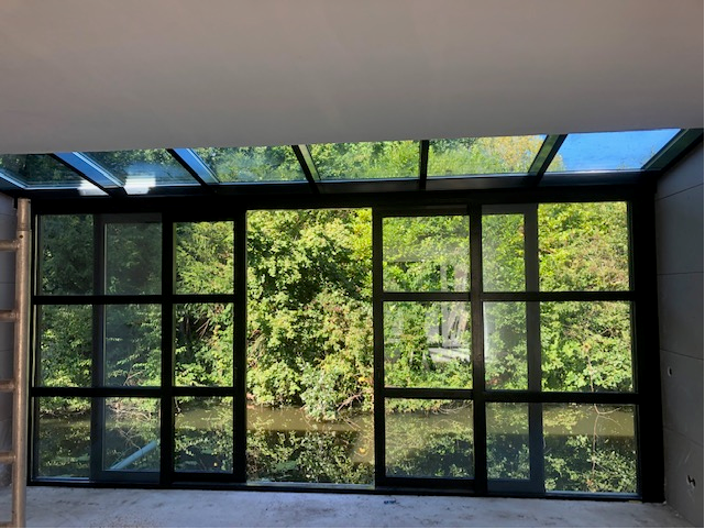 Serre met glazen dak en aluminium schuifpui met uitzicht op water