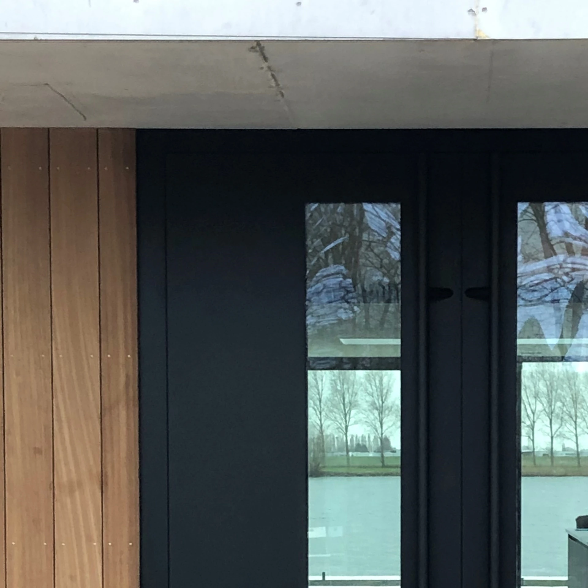 Zwarte aluminium deur naast houten gevelbekleding