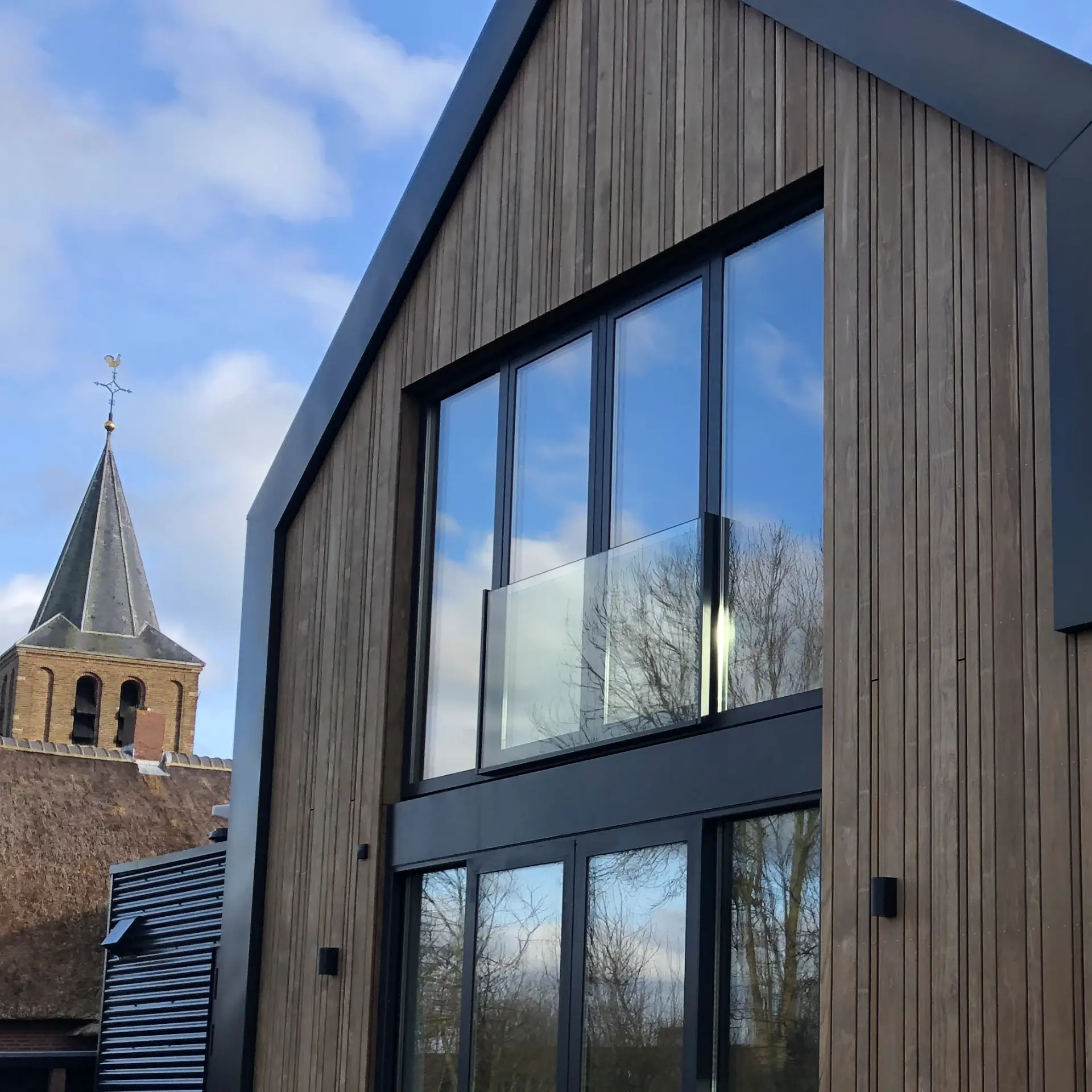 Schuurwoning met houten gevel, hoge aluminium puien en glazen balustrade